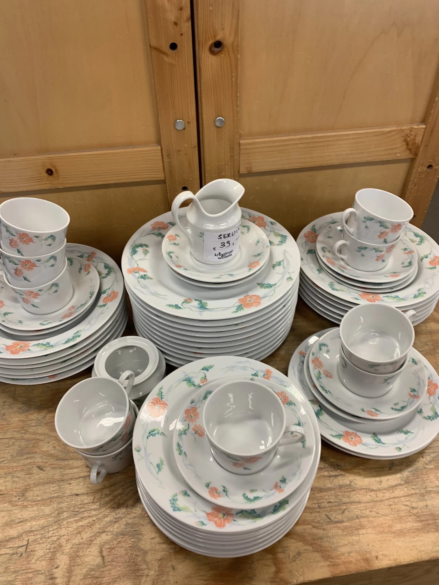 Uitgestald servies met bloemmotief: stapels borden, kopjes, schotels en een kannetje.