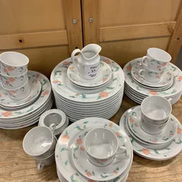 Uitgestald servies met bloemmotief: stapels borden, kopjes, schotels en een kannetje.