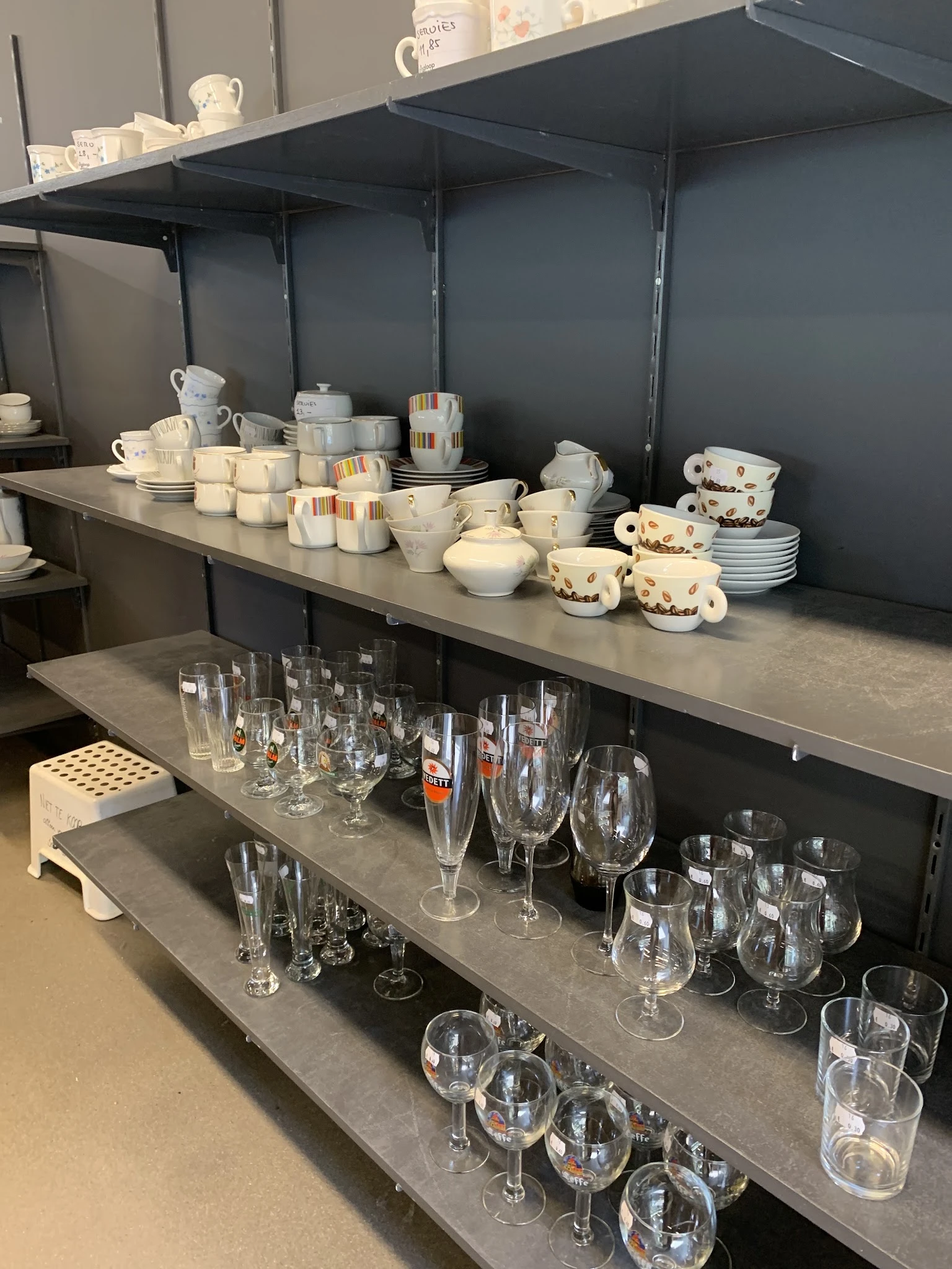 Stellingen met serviesgoed, glazen en huishoudartikelen uitgestald in de winkel
