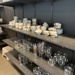 Stellingen met serviesgoed, glazen en huishoudartikelen uitgestald in de winkel
