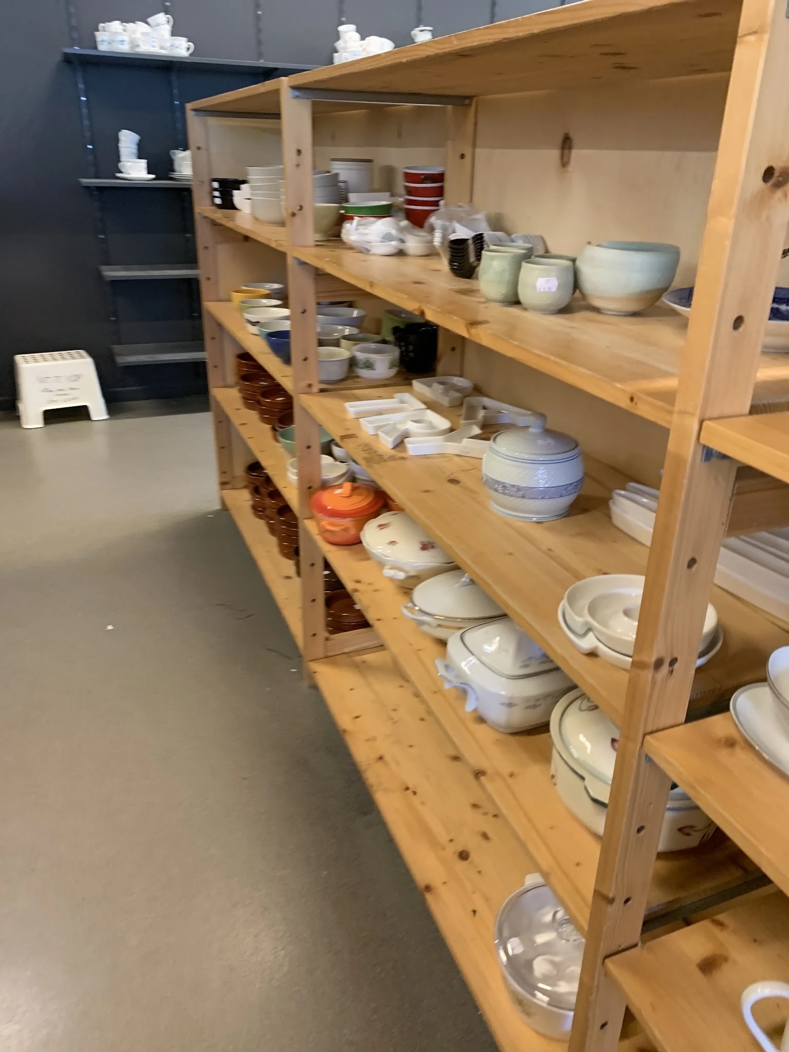 Houten stellingen met serviesgoed, schalen en aardewerk in verschillende kleuren en stijlen