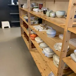 Houten stellingen met serviesgoed, schalen en aardewerk in verschillende kleuren en stijlen