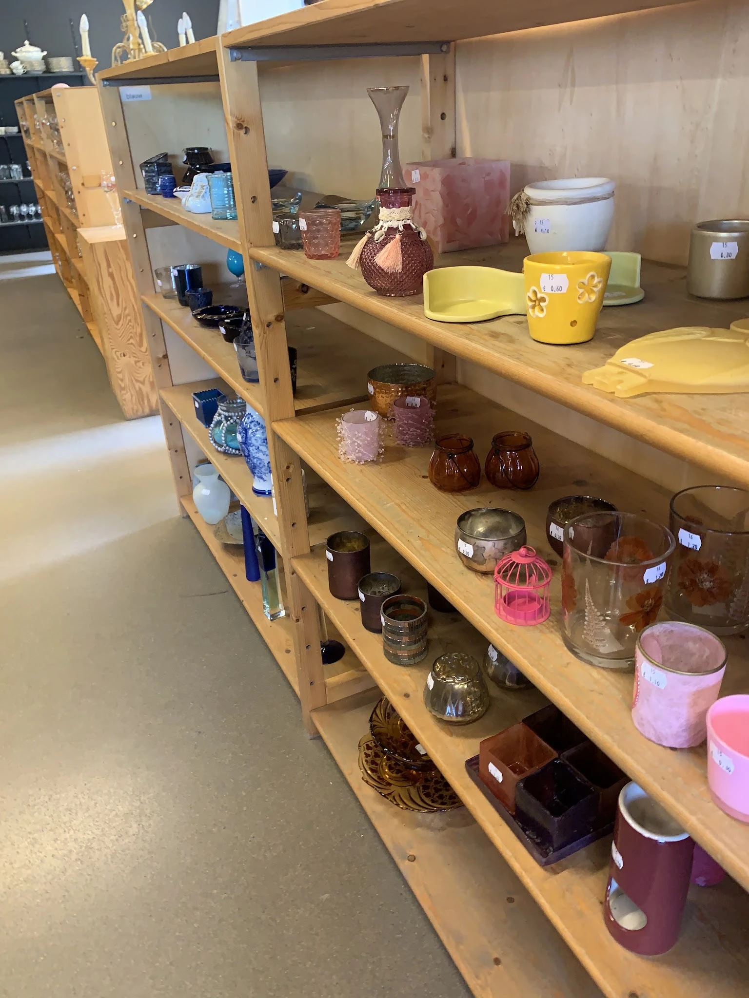 Houten stellingen met assortiment huishoudartikelen: glazen potten, bekers, kaarsen en serviesgoed
