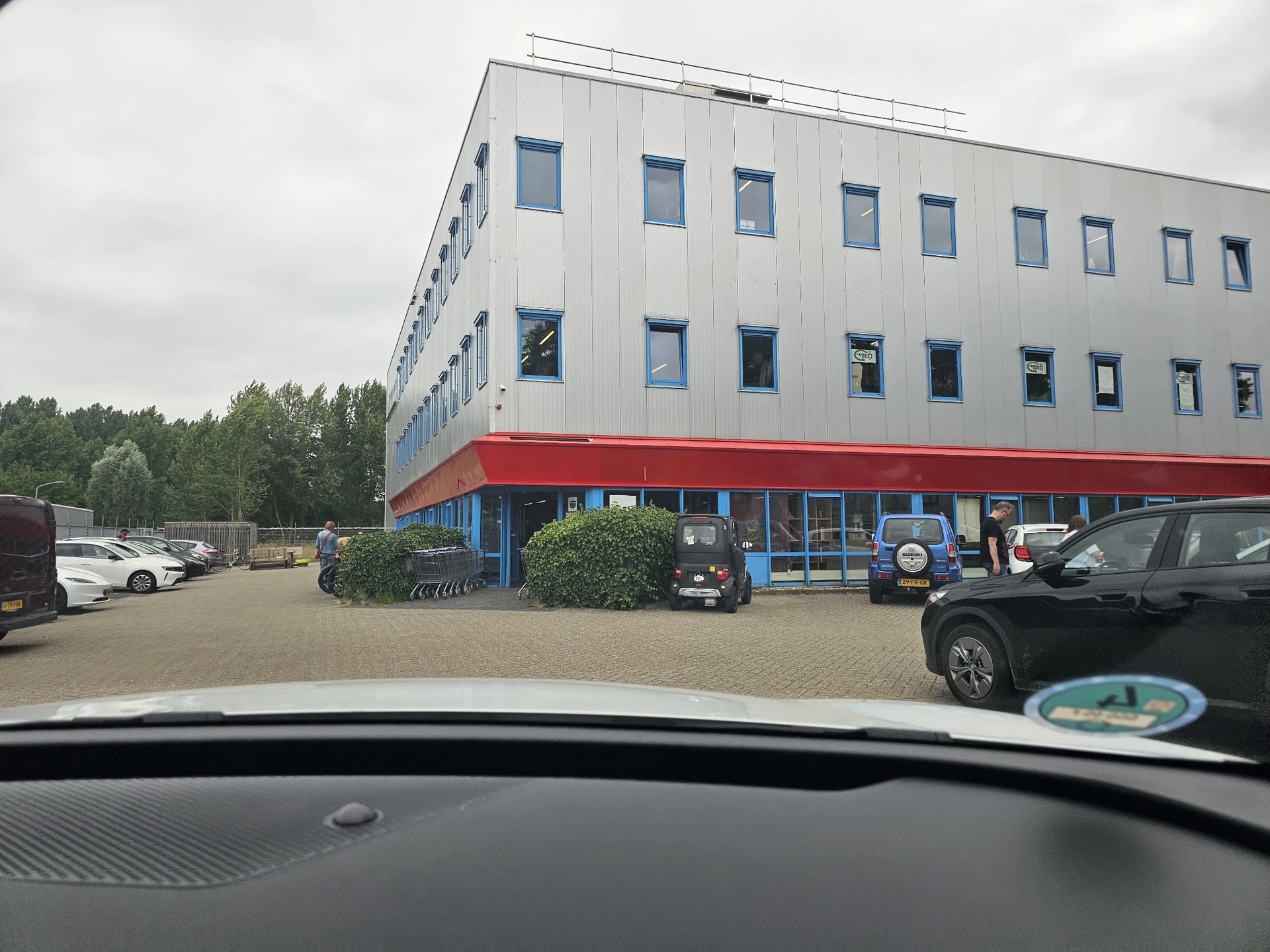 Voorgevel van een moderne kringloopwinkel met wit bovengedeelte, rode onderzijde en parkeerplaats ervoor