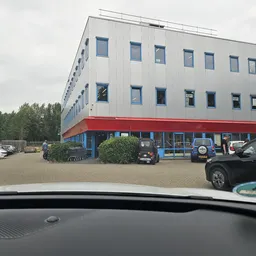 Voorgevel van een moderne kringloopwinkel met wit bovengedeelte, rode onderzijde en parkeerplaats ervoor