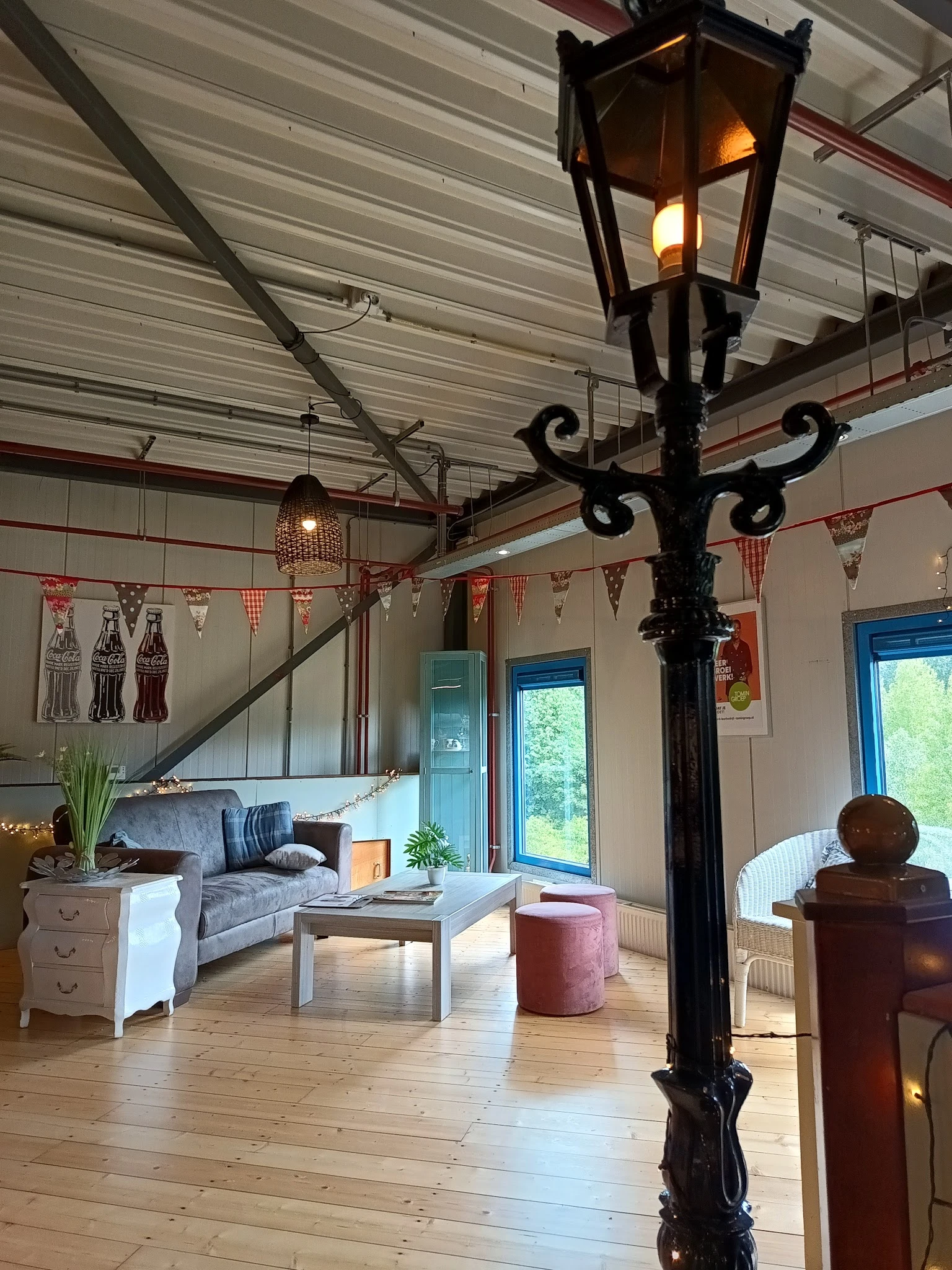 Woonkamer-achtige inrichting met bank, tafel, poef en decoratieve elementen in een ruimte met hoog plafond