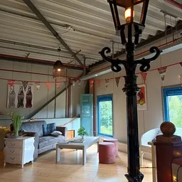 Woonkamer-achtige inrichting met bank, tafel, poef en decoratieve elementen in een ruimte met hoog plafond