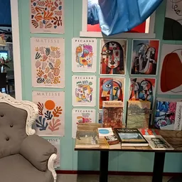 Wand met kunstafdrukken van Matisse en Picasso, fotolijsten, boeken en decoratieve items op een houten tafel, naast een vinta
