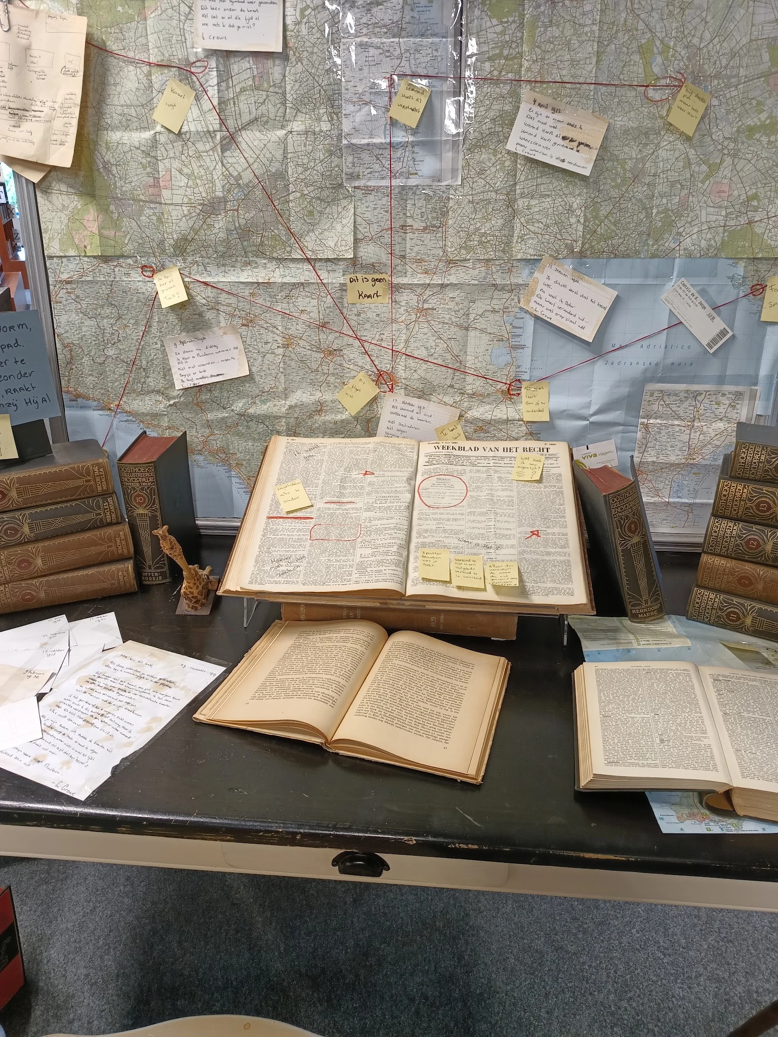 Tafel met opengeslagen antieke boeken, kaarten en notities in een winkelinterieur met boekenrekken op de achtergrond