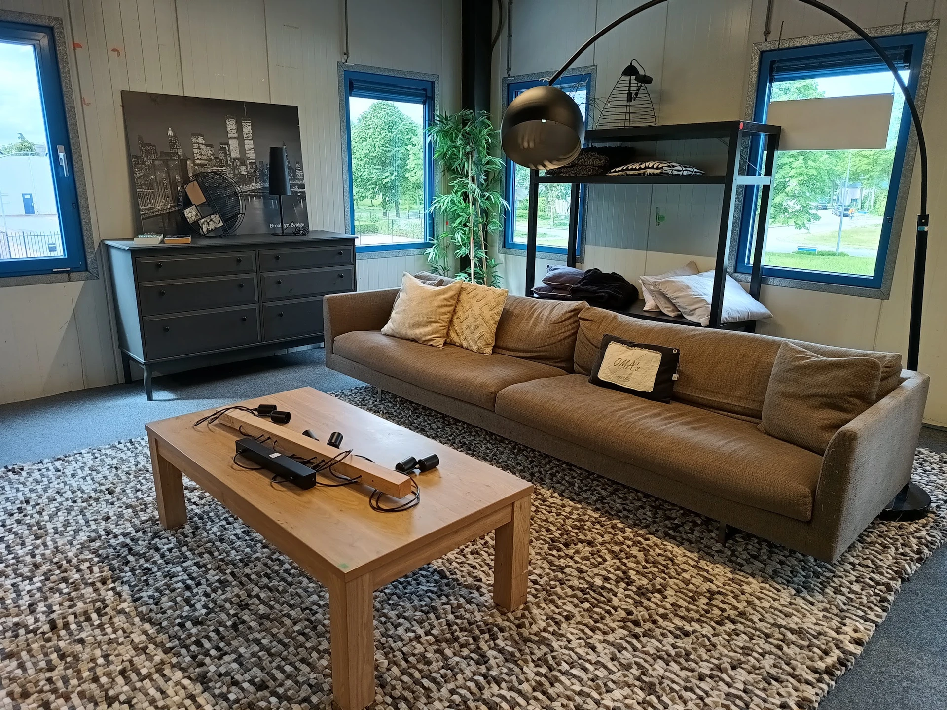 Woonkamer-display met bruin leren bank, houten tafel, zwarte dressoirkasten en bovenbed in een kringloopwinkel