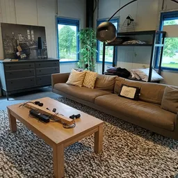 Woonkamer-display met bruin leren bank, houten tafel, zwarte dressoirkasten en bovenbed in een kringloopwinkel