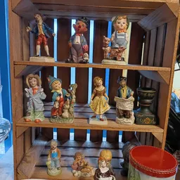 Houten vitrinekast met collectie antieke poppen en beeldjes op drie niveaus