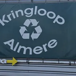 Donkerblauwe gevel met wit logo van Kringloop Almere en recyclesymbool, gele pijl eronder