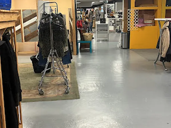 Winkelvloer van kringloopwinkel met kledingrekken, stellingen en gele kasten, grijs betonnen vloer