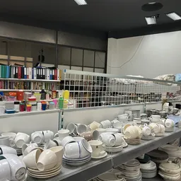 Tafels vol serviesgoed, kopjes, schotels en borden in wit en beige, met boekenkasten en ander aanbod op de achtergrond