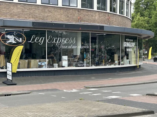 Storefront van een kledingwinkel met grote ramen en zwarte gevel, gele banner links, straat met tegels zichtbaar