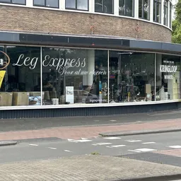 Storefront van een kledingwinkel met grote ramen en zwarte gevel, gele banner links, straat met tegels zichtbaar