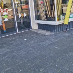 Voorkant van kringloopwinkel met donkere gevel, glazen deur en ramen met enkele spullen zichtbaar