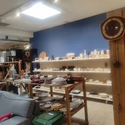Uitgestalde serviesgoed, vazen en huishoudelijke artikelen op witte stellingen en houten tafels in de winkel