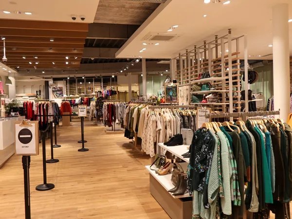 Ruim tweedehands kledingwinkel met rekken vol kleding, houten vloer en moderne inrichting