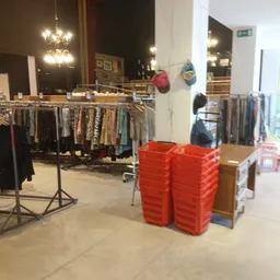 Winkelinterieur met kledingrekken en rode plastic kratten op de vloer