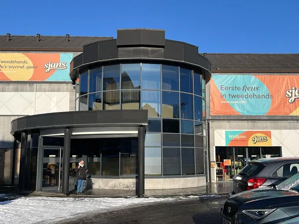 Moderne gevel van kringloopwinkel met zwarte ronde uitbouw, grote glazen ramen en gekleurde banners met 'suns' logo