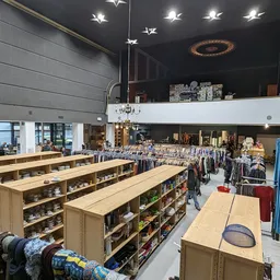 Ruim winkelinterieur met houten stellingen vol spullen, kledingrekken en decoratie-items onder spotverlichting