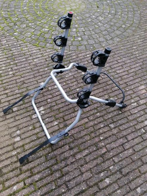 Witte fietsendrager met zwarte bevestigingsklemmen op bakstenen ondergrond