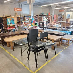 Werkruimte met tafels en stoelen in kringloopwinkel, omgeven door boeken en spullen