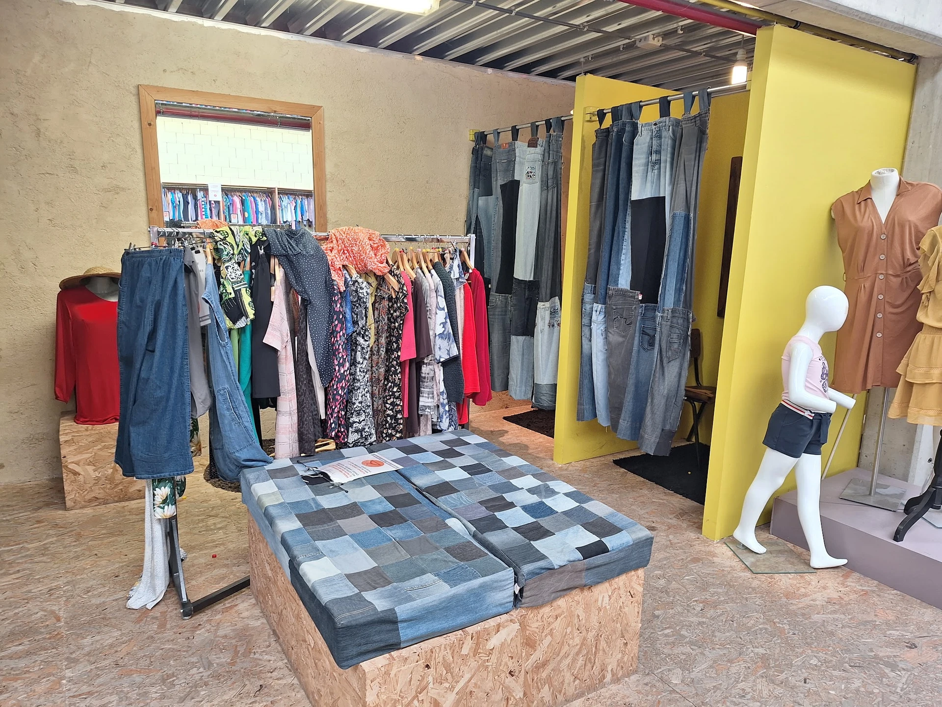 Winkelvloer met kledingrekken, etalagepoppen en uitgestalde tweedehands kleding in verschillende kleuren