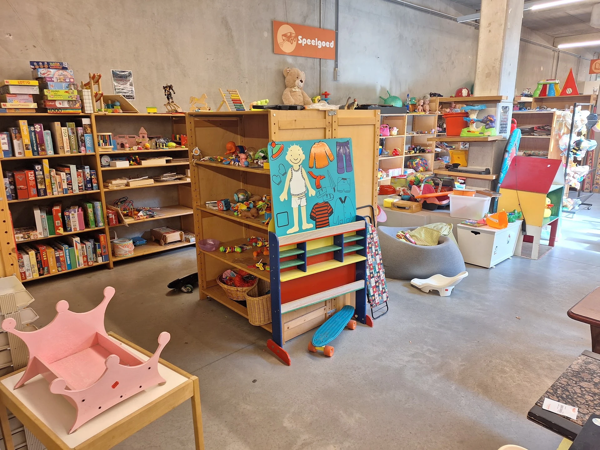 Speelgoedafdeling in kringloopwinkel met houten speelgoed, boeken, speeltoestellen en opbergkisten op betonvloer