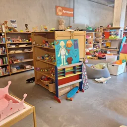 Speelgoedafdeling in kringloopwinkel met houten speelgoed, boeken, speeltoestellen en opbergkisten op betonvloer