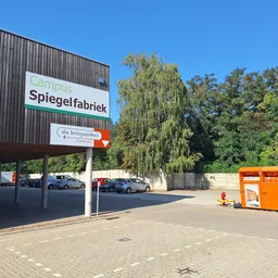 Voorgevel van kringloopwinkel met bord 'Spiegelfabriek', parkeerplaats en oranje containers