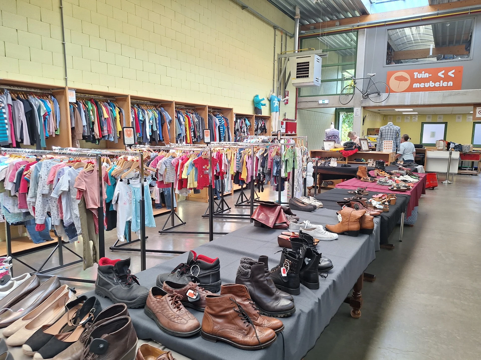 Uitgestalde tweedehands kleding op rekken en tafels, met schoenen en accessoires in de voorgrond