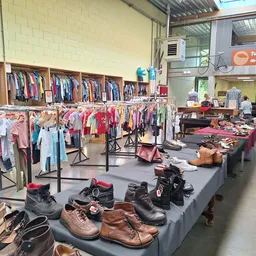Uitgestalde tweedehands kleding op rekken en tafels, met schoenen en accessoires in de voorgrond