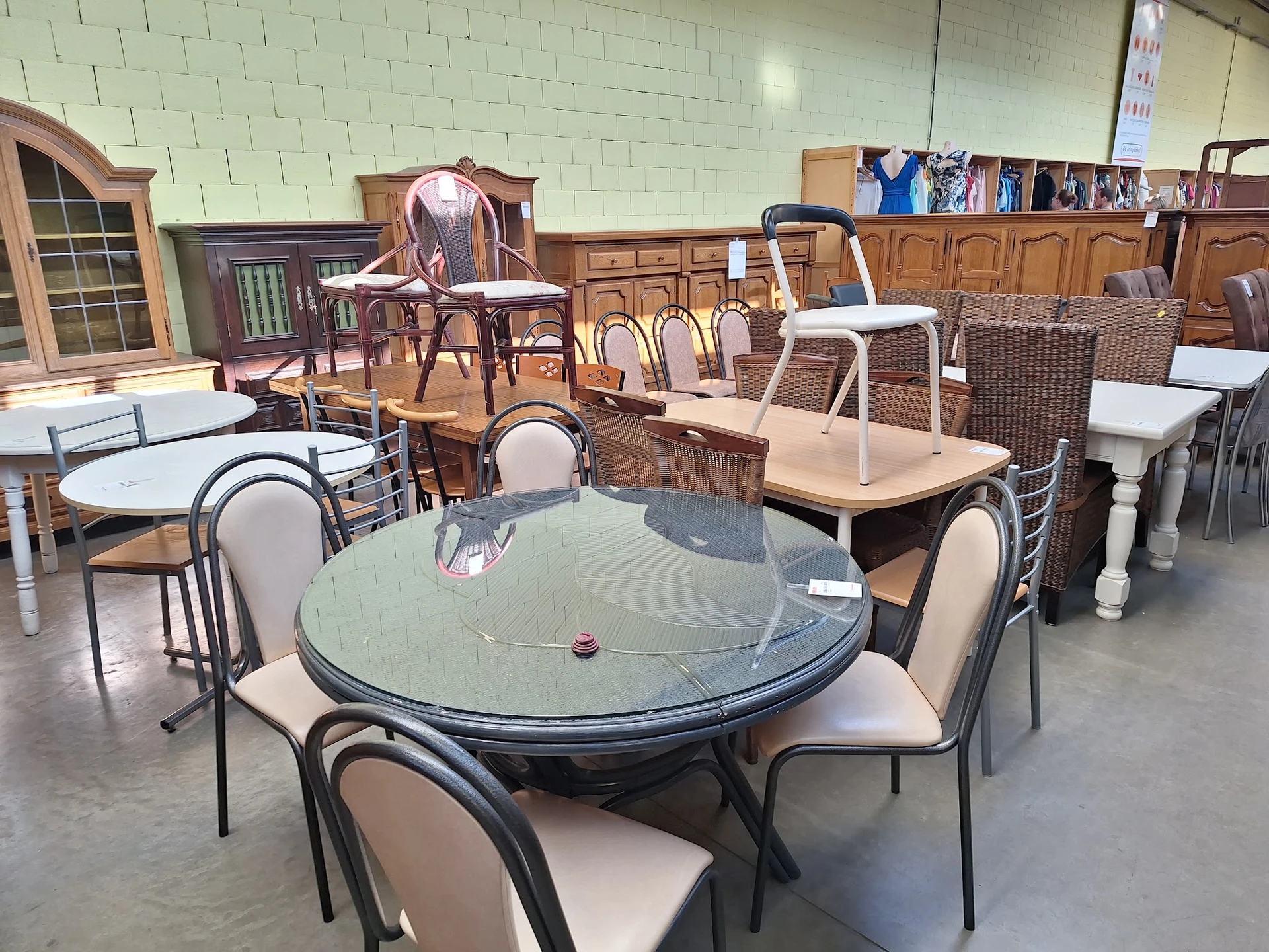 Meubels in een kringloopwinkel: ronde glazen eettafels met stoelen, houten kasten en diverse zitmeubels