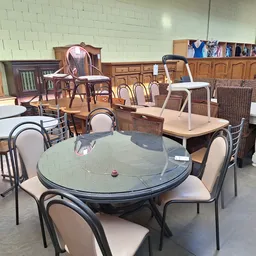 Meubels in een kringloopwinkel: ronde glazen eettafels met stoelen, houten kasten en diverse zitmeubels