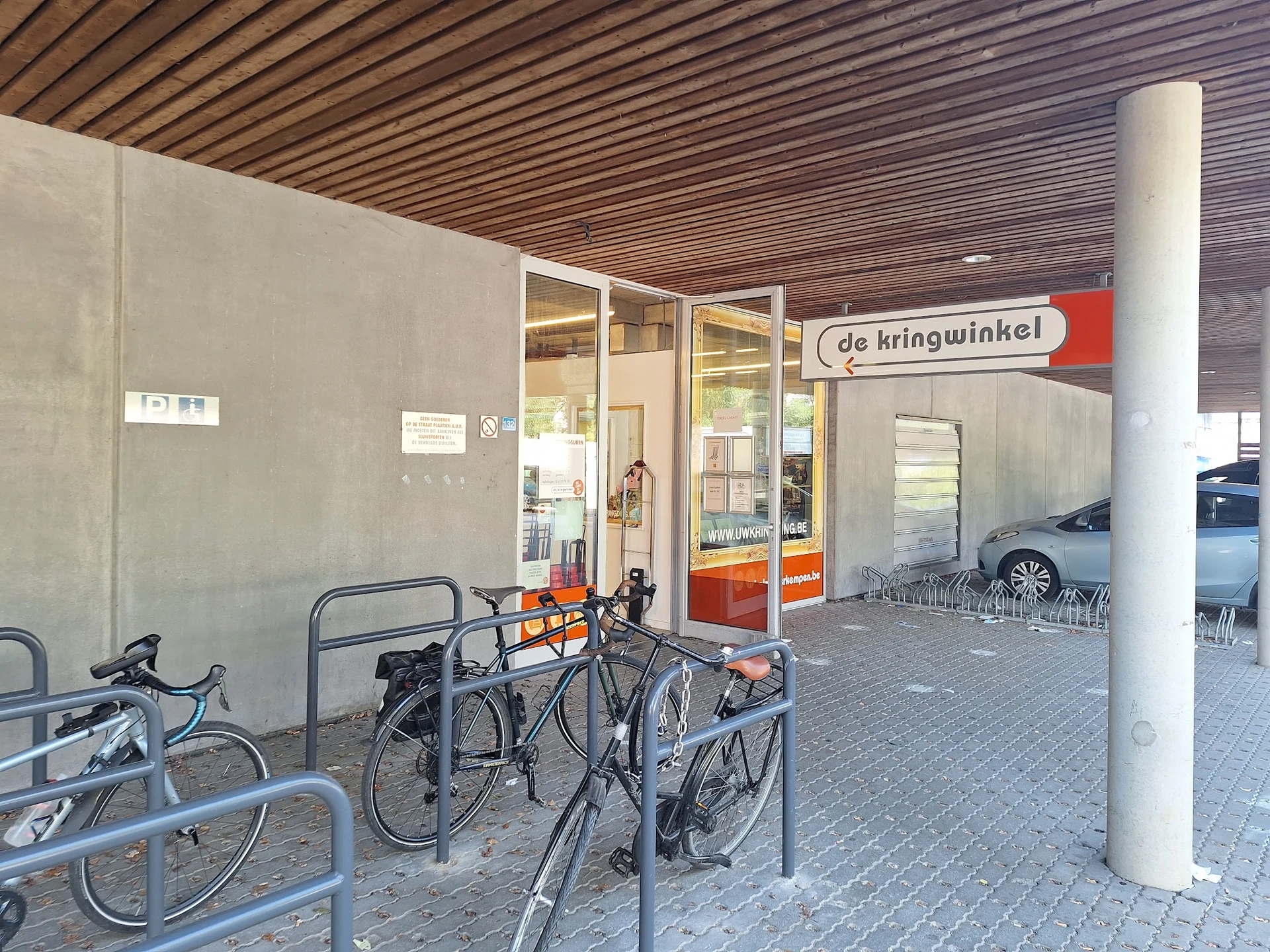 Winkelfront met glazen deuren en 'de kringwinkel' naambordje, fietsenrek daarvoor