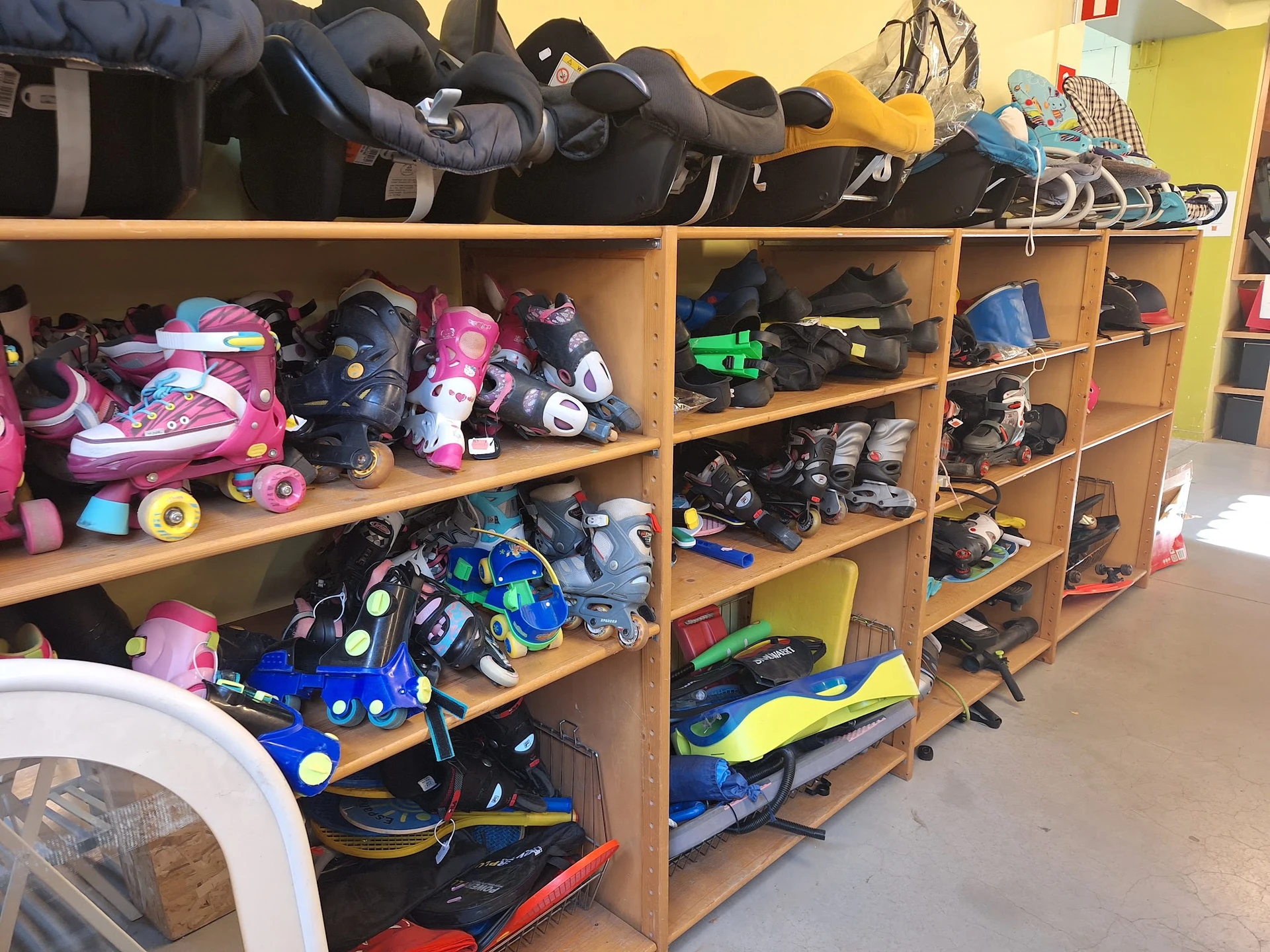 Houten stellingen vol met tweedehands sportuitrusting en rolschaatsen, roze en blauwe items zichtbaar