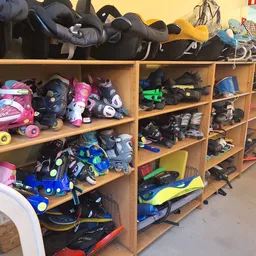 Houten stellingen vol met tweedehands sportuitrusting en rolschaatsen, roze en blauwe items zichtbaar