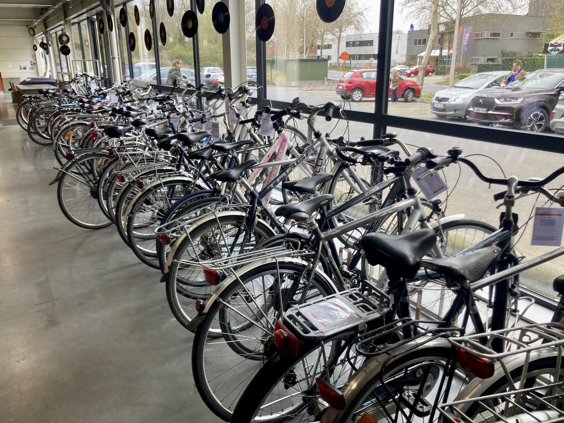 Rij van tweedehands fietsen in verschillende kleuren opgesteld onder afdak voor de winkel