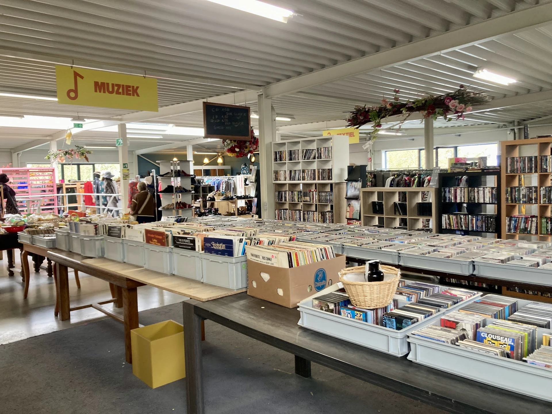 Winkelvloer met tafels vol met cd's, boeken en diverse tweedehands artikelen; boekenkasten op de achtergrond