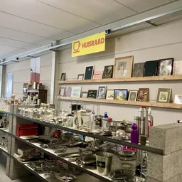Vitrinekast met huishoudelijke artikelen en serviesgoed in kringloopwinkel, met wandrek met foto's en posters op achtergrond
