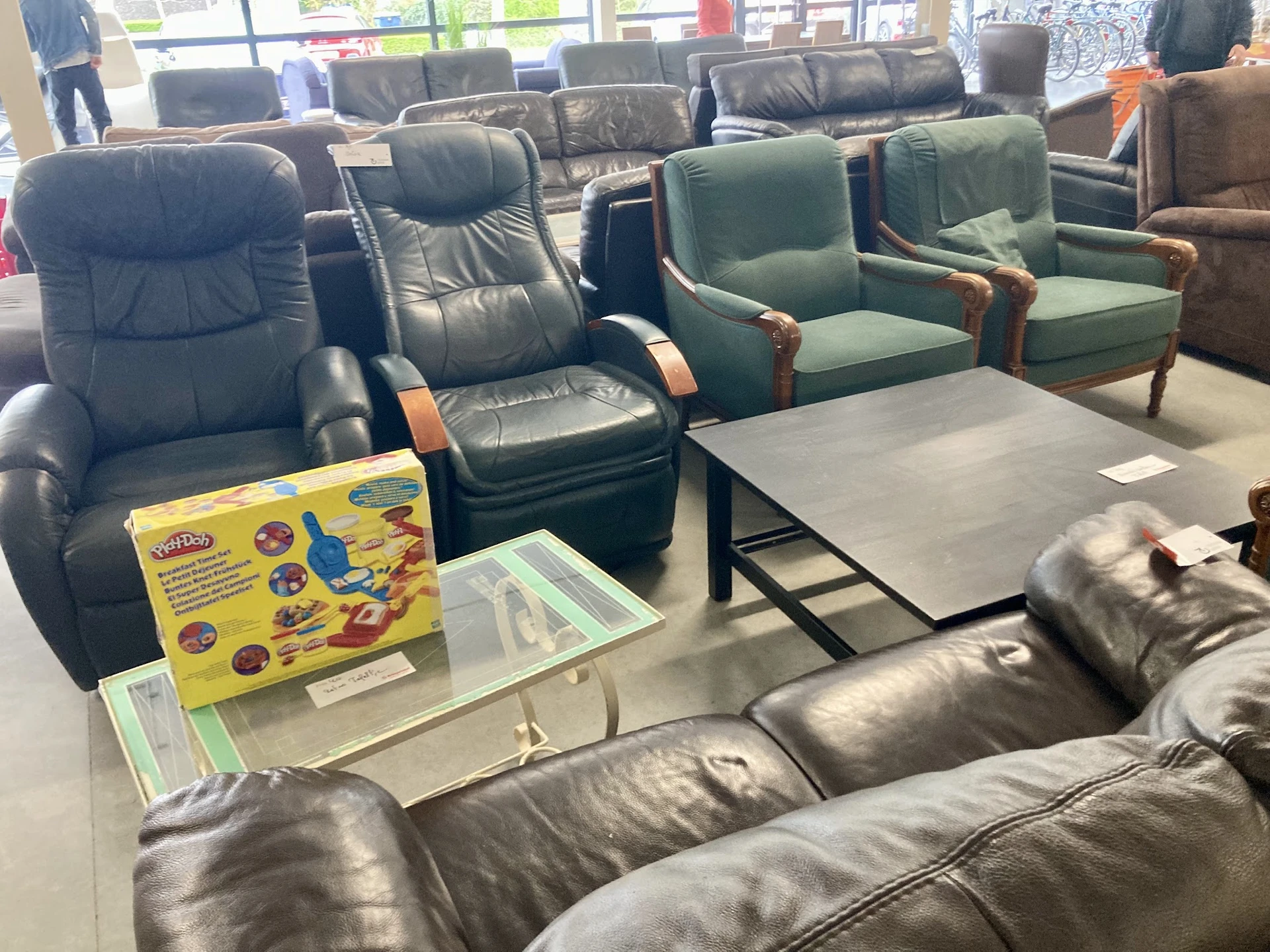 Tweedehands meubels uitgestald in kringloopwinkel: leunfauteuils, stoelen en tafel in verschillende kleuren