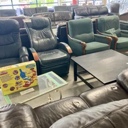 Tweedehands meubels uitgestald in kringloopwinkel: leunfauteuils, stoelen en tafel in verschillende kleuren