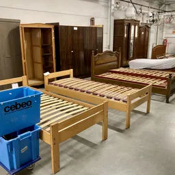 Uitgestalde houten bedden en kasten in het magazijn van de kringloopwinkel