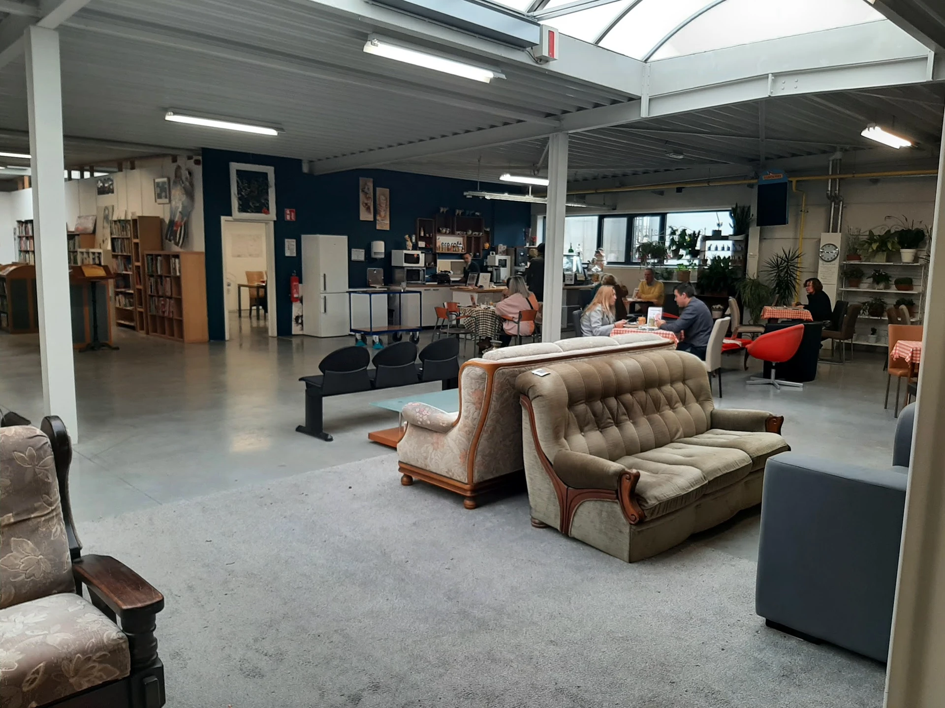 Ruime winkelvloer met vintage meubels, fauteuils en banken, stellingen met spullen op de achtergrond, hoge plafonds met dagli