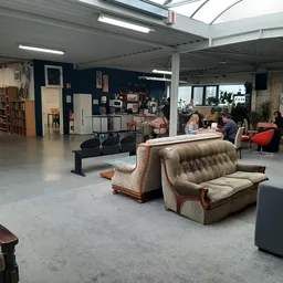 Ruime winkelvloer met vintage meubels, fauteuils en banken, stellingen met spullen op de achtergrond, hoge plafonds met dagli