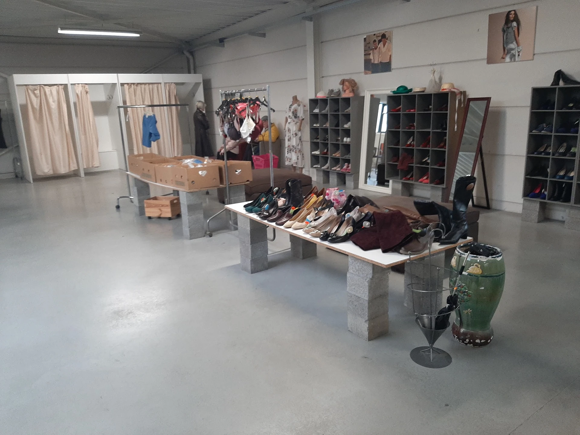 Winkelvloer met uitgestalde kleding op tafels, stellingen met schoenen en diverse spullen tegen de muur