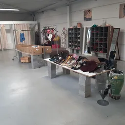Winkelvloer met uitgestalde kleding op tafels, stellingen met schoenen en diverse spullen tegen de muur